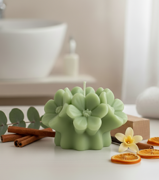 Green succulent-shaped candle on a bathroom counter with eucalyptus, oranges, and cinnamon sticks.