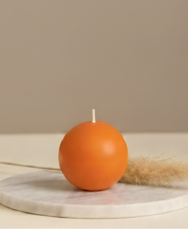 Orange spherical candle on a marble coaster with a beige background